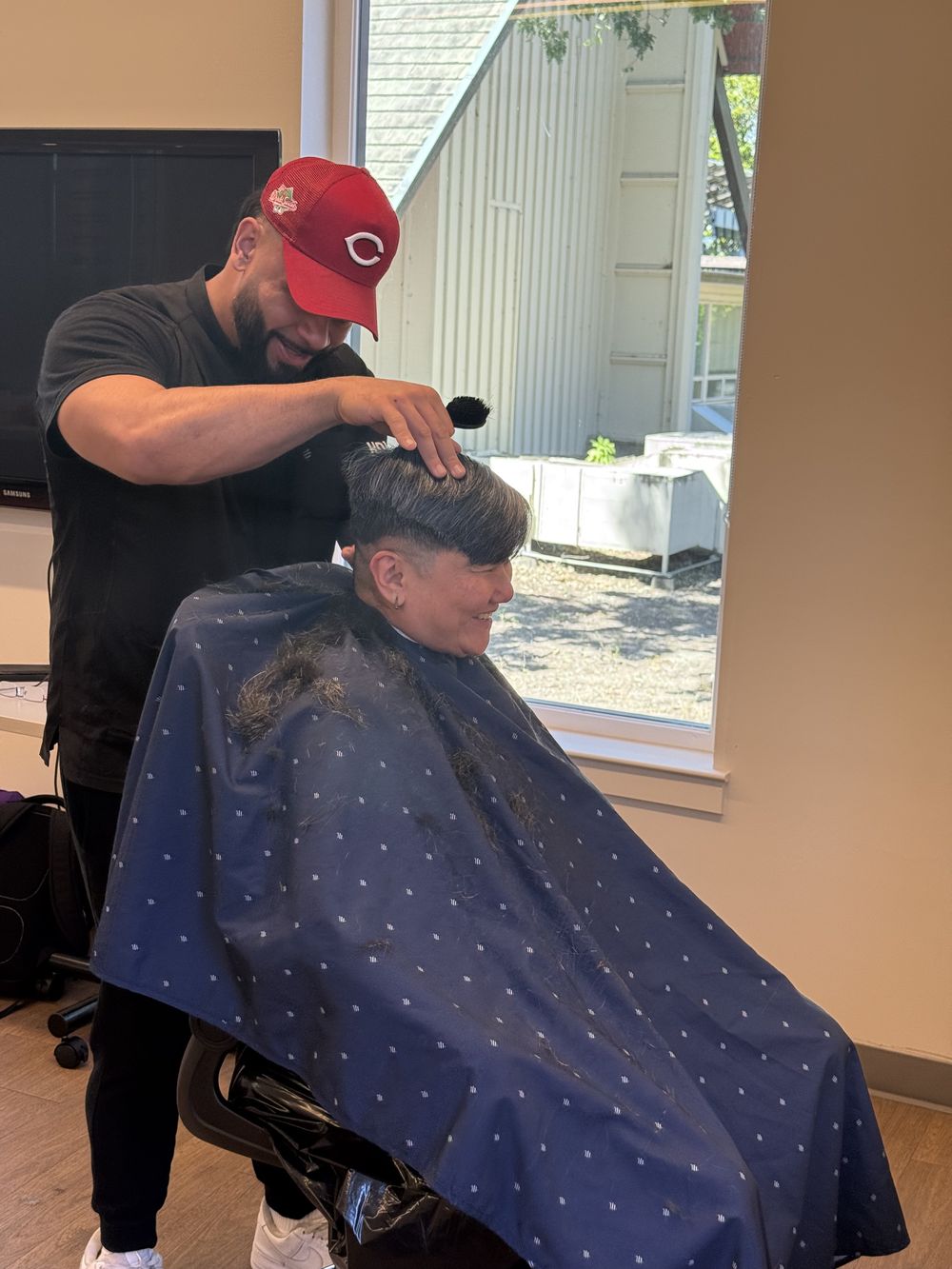 A volunteer barber giving a smiling community member a fresh haircut at the Trinity Center event.